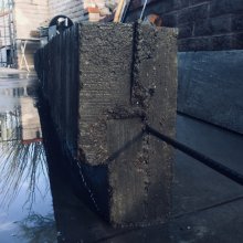 picture of a concrete bench segment with a piece of rebar poking into the foreground and out of frame. water puddle on left with reflections of branches and sky.